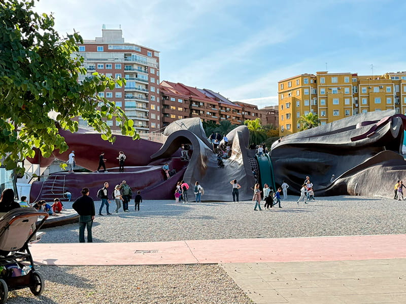 Панорамный вид на Parque Gulliver в Valencia: большая фигура Гулливера-аттракциона и дети на площадке, на фоне жилые дома.